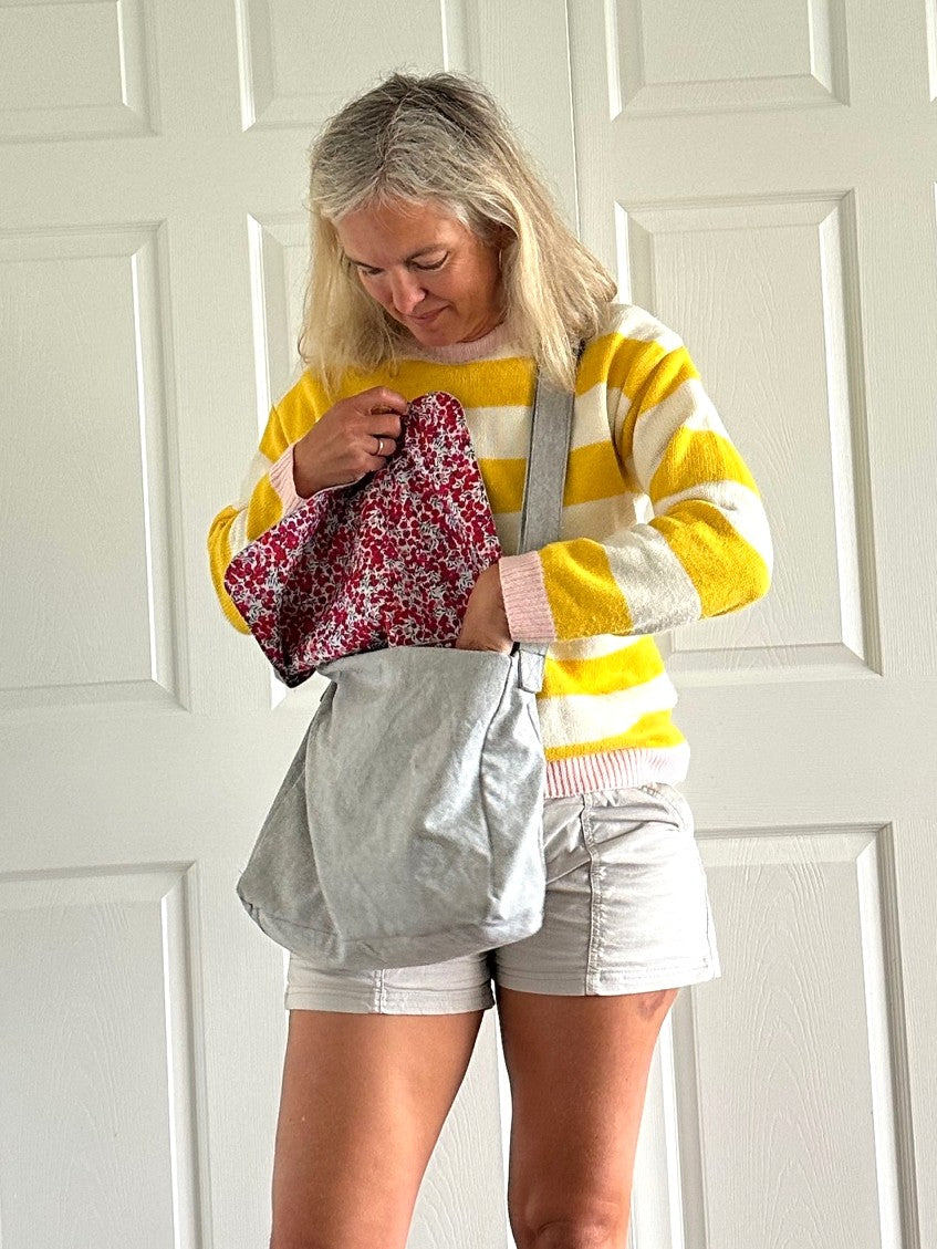 Woman wearing a yellow and white striped sweater with gray bag with floral lining.