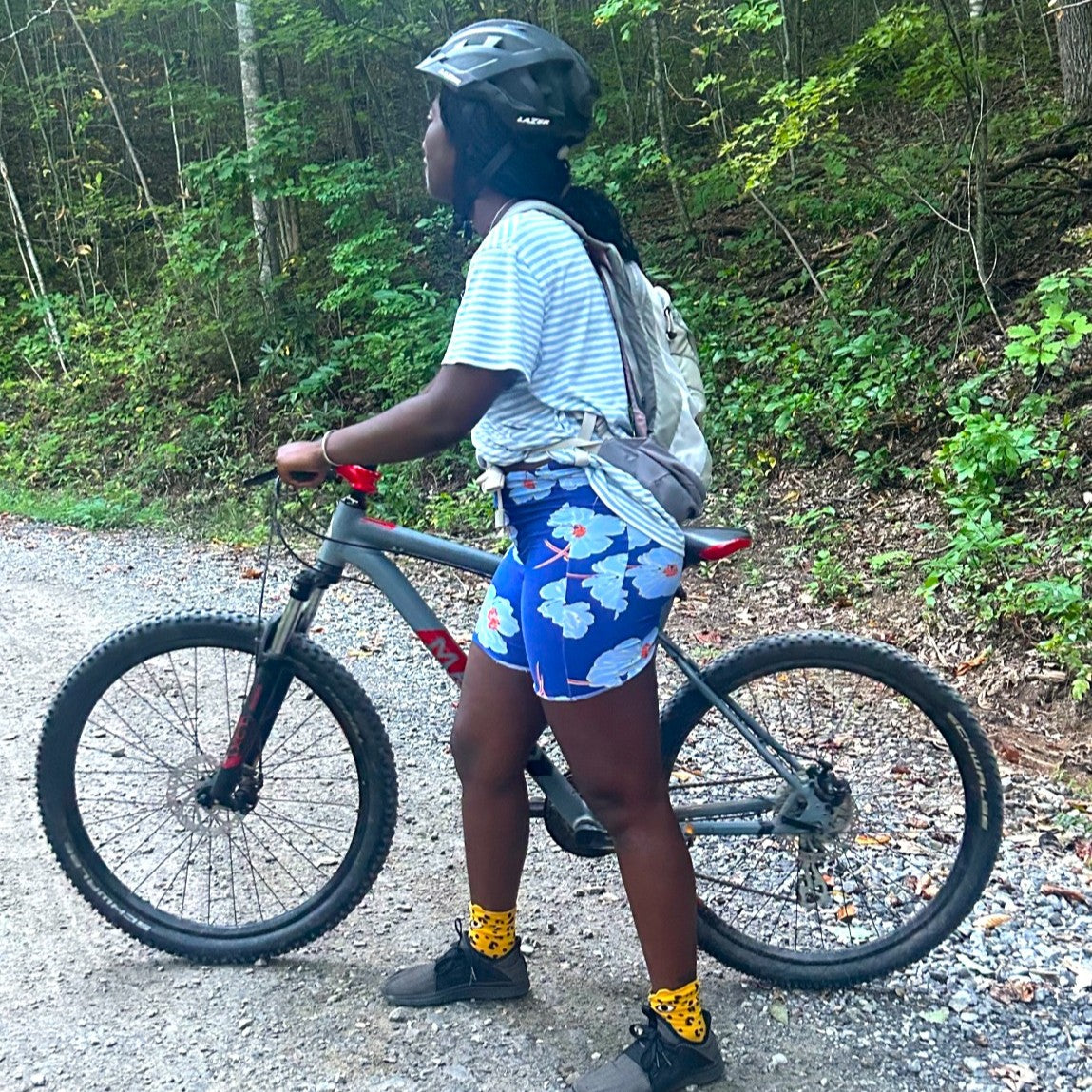 Person wearing blue floral biking shorts with a bicycle on a forest path