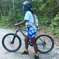Person wearing blue floral biking shorts with a bicycle on a forest path