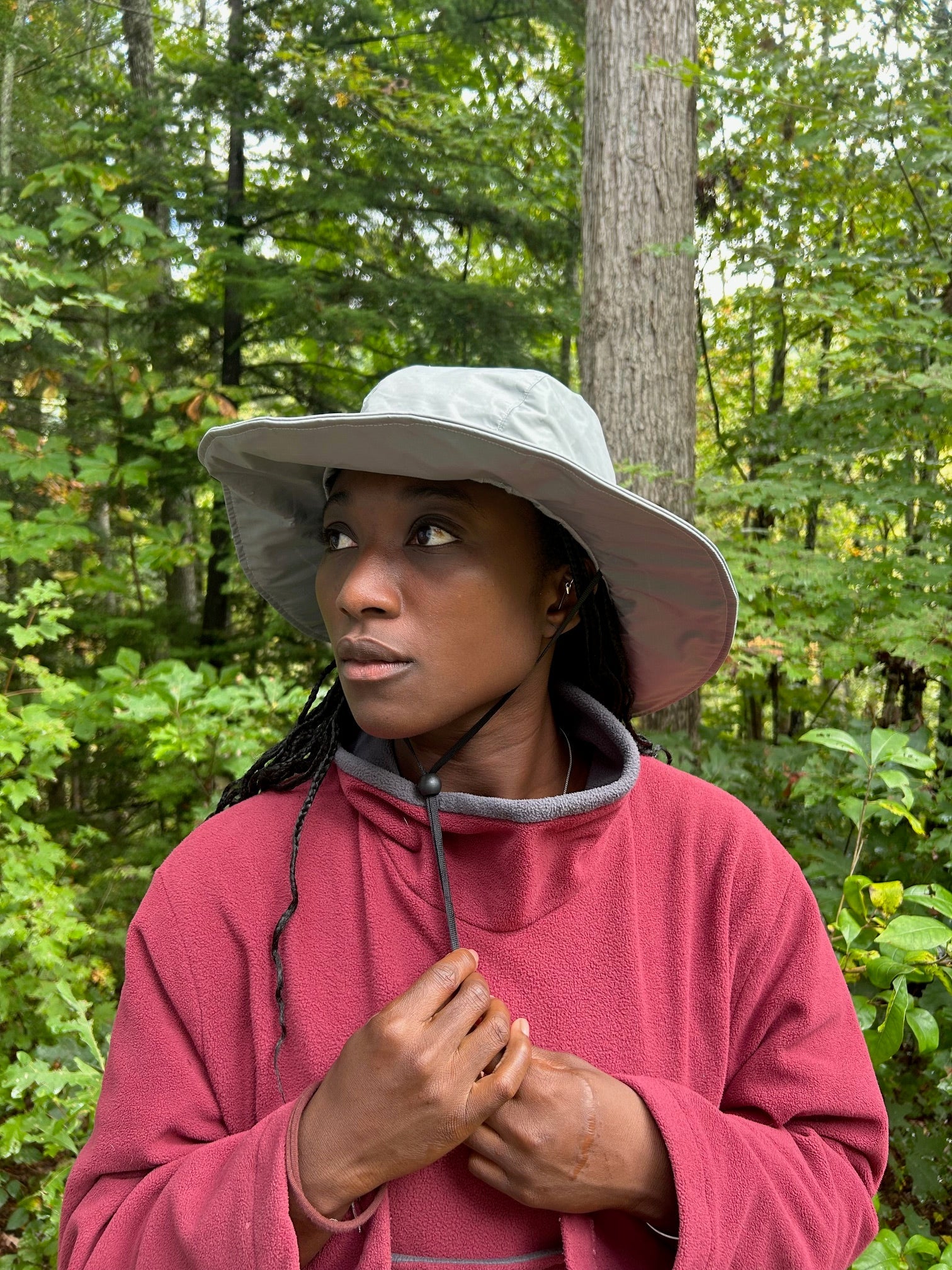 Woman wearing a grey hat and red fleece sweater in a fores setting.
