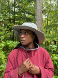 Woman wearing a grey hat and red fleece sweater in a fores setting.
