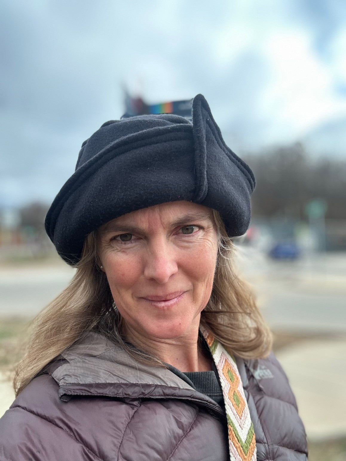Woman wearing a black roll brim hat outside.  Hat has an overlap with corner on brim.
