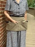Person wearing a floral shirt and patterned pants with a beige toll belt against a brick wall.