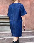 Person wearing a blue denim dress standing on stone steps with a red-brown wall in the background.
