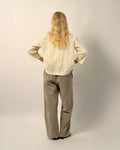 Person wearing a beige shirt and gray pants against a plain background